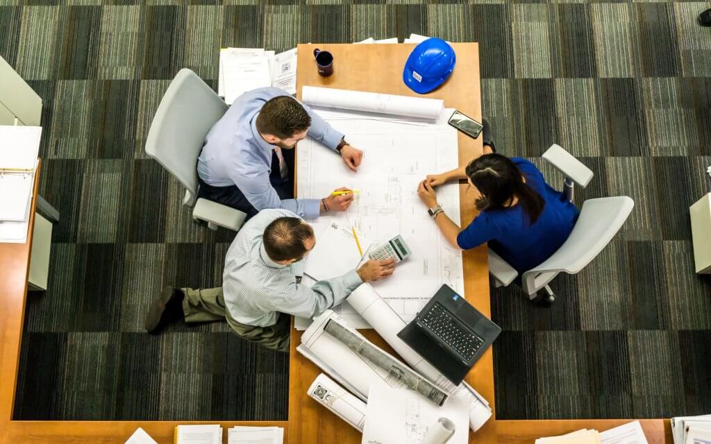 A shot of three people from overhead, surrounding a desk and working together. Used to illustrate what GRC is and how the three components work together.