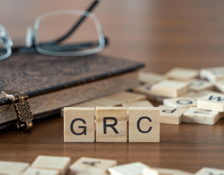 Wooden letters spelling GRC next to a notebook and glasses. Other letters are scattered.